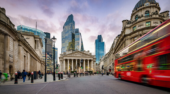 Sunset view of the City of London, England, with commuter and street traffic in front of the Bank of England