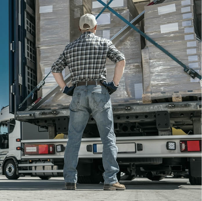 Trucker standing and looking at the rear of a trailer truck loaded with cargo.