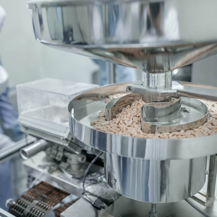 Automated tablet production line in a cleanroom facility with staff in protective suits, showing modern pharmaceutical packaging