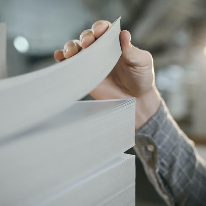 Close up of man putting stack of paper in printing machine at publishing shop, copy space.
