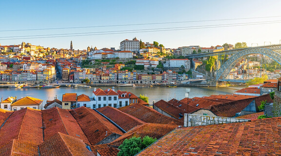 Panoramic view of Porto city Ribeira district with red rooftops, Douro River and Dom Luis Bridge at sunrise, Portugal. Oporto old town with Portuguese architecture. Travel and tourism in Europe