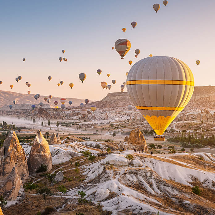 Beautiful panoramic view of the valley in Cappadocia with magical flying balloons and at sunset. Travel and vacation in Turkey.
