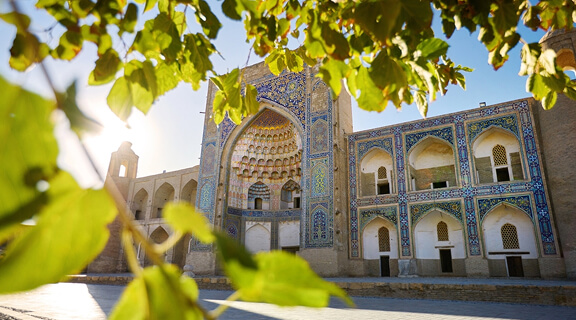Beautiful view of landmark exterior Madrasah of Abdulaziz Khan framed with green leaves tree in old city of Bokhara, Uzbekistan