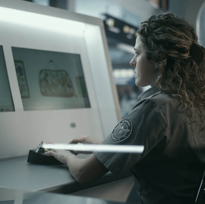 Concentrated Female Officer in Uniform Manages Scanning System at Security Checkpoint While Travelers Pass in Background. Reliable National Security, Professional Duty, Efficient Customs Clearance.